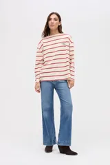 Remera de manga larga con diseño a rayas horizontales en color crema y rojo. Presenta un corte holgado, cuello redondo y un pequeño bordado en el pecho.