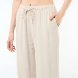 Pantalón de lino color beige, de corte ancho y relajado, con cintura elástica con cordón de ajuste y bolsillos laterales.