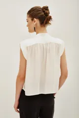 Camisa de corte oversize color negro, con cuello mao, mangas cortas y botones ocultos. Presenta un pin metálico decorativo con strass en el cuello.