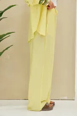 Pantalón de pierna ancha color amarillo pastel, de tiro medio con cintura elástica fruncida y cordón ajustable.