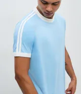 Remera de algodón color celeste con cuello redondo y bordes de mangas en color blanco. Presenta diseño de rayas dobles blancas en los hombros y mangas.