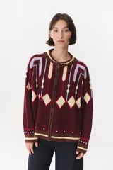 Campera tipo bomber tejida con diseño jacquard geométrico en tonos bordó, crema y celeste. Presenta cierre frontal completo, cuello redondo, mangas largas con hombros caídos y puños acanalados con rayas contrastantes.