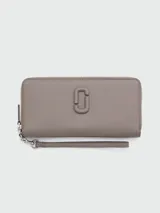 Billetera continental Marc Jacobs de cuero en color gris topo, con cierre perimetral, logo metálico frontal y correa de muñeca extraíble.