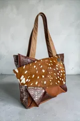 Cartera tipo shopper confeccionada en cuero con diseño patchwork en tonos marrones y animal print, asas de hombro en tono tostado y detalle de dije colgante metálico triangular.