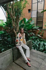 Chaqueta de algodón color crudo con cuello redondo, manga larga y bolsillos delanteros de plastrón. Presenta un diseño con bordados coloridos de flores y motivos abstractos a contraste, y cierre frontal con botones oscuros.