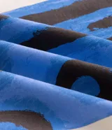 Remera de corte boxy confeccionada en algodón, con cuello redondo y manga corta. Presenta una estampa frontal con diseño artístico abstracto en tonos azules y marrones sobre un fondo claro.