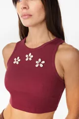 Musculosa de algodón en color bordó, de corte corto, con cuello redondo y detalles de flores decorativas aplicadas en el pecho.