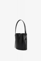 Bolso de mano tipo cubo color negro, de diseño estructurado y cilíndrico, confeccionado en cuero vacuno con acabado brillante. Cuenta con asa superior fija y correas laterales decorativas con hebillas metálicas plateadas.