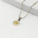 Conjunto compuesto por una cadena de eslabones redondos en plata y un dije circular con diseño de grecas en el borde y figura central en oro.