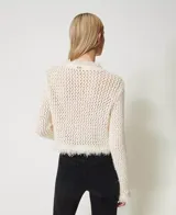 Sweater de punto calado color crema, con cuello redondo, manga larga, flecos en el ruedo y dos bolsillos de parche con botones metálicos con el logo de la marca.