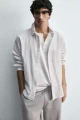 Camisa de corte relajado confeccionada en tejido de algodón con textura, diseño a rayas verticales, cuello abotonado, manga larga con puños y bolsillo de plastrón en el pecho.