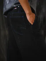 Pantalón de jean negro de corte amplio, inspirado en las bombachas de campo, con costuras a contratono en color azul y bolsillos Temblad.