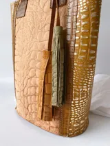 Bolso matero de cuero color beige con textura tipo piel de cocodrilo, detalles en cuero color marrón y borlas decorativas.