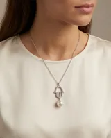 Collar de plata con cadena fina y dije en forma de mano de Hamsa decorado con circonias, acompañado por un dije de perla de río colgante.