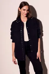 Sobrecamisa negra de algodón con corte oversize, cuello clásico, cierre frontal con botones a presión, dos bolsillos de parche en el pecho y apliques metálicos en cuello y solapa.