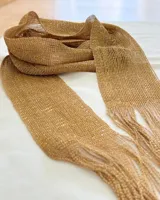 Bufanda dorada de tejido calado con flecos en los extremos.