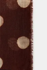 Pañuelo rectangular de lana con estampado de lunares en tonos claros sobre fondo marrón oscuro. Presenta bordes desflecados y una franja lisa en uno de los extremos.
