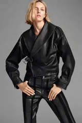 Chaqueta corta de piel 100% color negro, de estilo cruzado con cierre de hebilla lateral. Cuenta con cuello solapa ancho, manga larga con puños estructurados y forro interior.