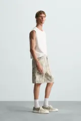 Bermuda relaxed fit confeccionada en tejido de algodón con efecto lavado. Presenta un diseño de cinco bolsillos, bolsillo multifunción en la pernera y tira lateral de estilo carpintero. Cuenta con cierre frontal con cremallera y botón.