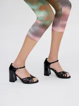 Sandalias de taco alto ancho con diseño retro, confeccionadas en charol negro. Presentan tiras delanteras múltiples entrelazadas, talón cerrado y una correa fina ajustable al tobillo con hebilla metálica.