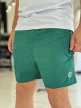 Short de baño verde liso, con cintura elástica y detalle de parche circular en el dobladillo inferior.