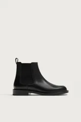 Bota tipo chelsea de piel lisa con elásticos laterales y horma redonda. Cuenta con suela de goma con ligero tacón y tirador trasero.