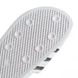 Ojotas Adidas Adilette Slide, color blanco con las tres bandas características de la marca en color negro sobre la banda superior. Diseño ergonómico con suela moldeada para mayor confort.