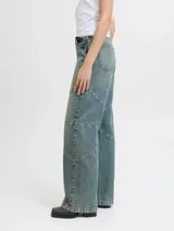 Jean wide fit de tiro medio, pierna curva y corte relajado, confeccionado en denim con lavado desgastado y costuras decorativas segmentadas.