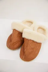 Pantuflas de cuero color tostado con interior de piel sintética, diseño bordado en la capellada y suela plana.