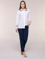 Camisa de crepe liviana y texturada color blanco, de silueta relajada y holgada, con cuello camisero clásico y puños con detalles de bordado de pasamanería con terminación deshilachada y aplique de perlas. Cuenta con cartera de botones oculta al frente y mangas largas.