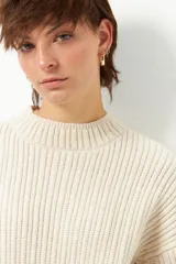 Polera color crema de tejido de punto con cuello alto y corte oversized.