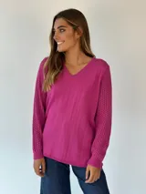 Buzo fucsia con cuello en V, cuerpo de tejido liso y mangas largas con diseño de punto calado texturizado.