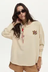 Buzo de felpa liviana color beige, con mangas largas, cuello redondo y bordado artesanal en el pecho.