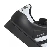 Championes Adidas modelo Superstar, color negro con las icónicas tres tiras laterales y detalle en el talón en color blanco. Presenta la clásica puntera de goma reforzada y suela de plataforma plana.