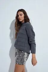 Sweater de punto gris con cuello a la base y diseño de trama geométrica en relieve. Presenta un calce relajado con mangas largas y puños tejidos.