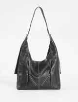 Cartera hobo negra de cuero sintético con costuras blancas decorativas y múltiples cierres diagonales en el frente. Tiene una correa de hombro ajustable.