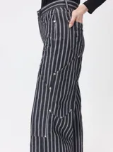 Pantalón de tiro medio y pierna ancha confeccionado en denim de algodón grueso. Presenta un diseño a rayas verticales en tonos azul y celeste, con costuras en contraste color rojo, bolsillos laterales tipo cargo y remaches metálicos.