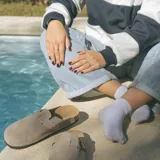 Zuecos de cuero gamuzado color beige, con plantilla anatómica de corcho, suela de goma negra y hebilla lateral ajustable.