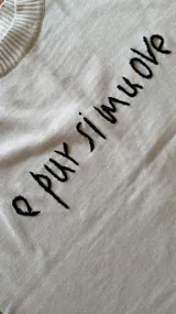 Sweater oversized crudo de tejido de punto, con hombros caídos y mangas largas. Presenta líneas negras en contraste en los hombros, bordado artesanal con la frase "e pur si muove" en el frente y aberturas laterales en el dobladillo.