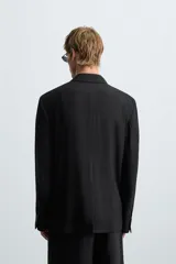 Blazer negra de corte relaxed fit, confeccionada en tejido con mezcla de viscosa. Tiene cuello con solapas de pico, manga larga con puños abotonados, bolsillos de vivo en pecho y cadera, abertura en el centro de la espalda y cierre frontal cruzado con botones.