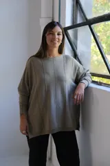 Sweater de punto con acabado brillante en tono verde oliva, de corte holgado y diseño con costuras verticales decorativas. Presenta cuello redondo y mangas largas con puños ajustados.