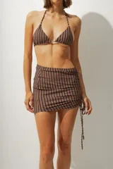 Falda corta tipo pareo con diseño de rayas verticales en tonos azul y negro. Presenta un lateral fruncido con cordón ajustable que permite regular el largo y el ajuste de la prenda.