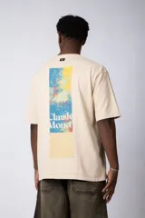 Remera de corte oversize color beige, confeccionada en algodón grueso. Presenta una estampa frontal pequeña con diseño artístico abstracto en tonos azules y amarillos.