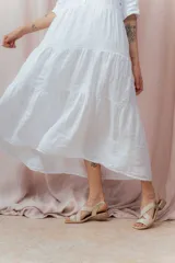 Vestido midi blanco de lino, con cuello camisero, botonera frontal y mangas 3/4. Presenta un calce relajado con frunces en la cintura.