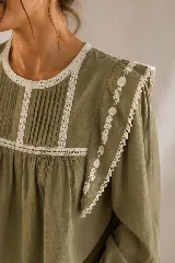 Blusa color tostado con cuello redondo, mangas largas abullonadas con puños elastizados, y detalles de puntillas y bordados en el frente y hombros.