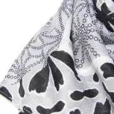 Pashmina de tela liviana con estampado floral en tonos blanco, gris y negro, con bordes decorados con patrones geométricos.