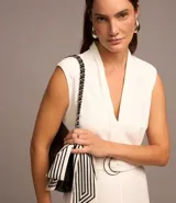 Mono largo de crepé color blanco, sin mangas, con cuello en pico, hombreras, pliegues, trabillas y cinturón con hebilla de aro doble.