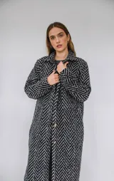 Tapado largo estilo chemise confeccionado en lana italiana tejida con patrón de espiga en color negro y gris. Presenta cierre frontal con botones y bolsillos con solapa.