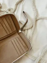 Billetera de cuero color visón con diseño acolchado de costuras cuadradas y cierre metálico perimetral.