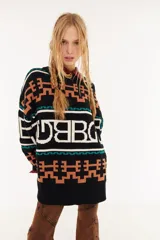 Sweater de punto oversize con diseño de intarsia geométrica y letras en tonos marrón, amarillo y rosado. Presenta cuello redondo, mangas largas y puños acanalados.